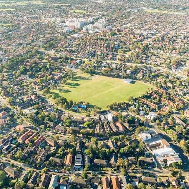 Aerial view of a large green sports field surrounded by residential houses and trees.