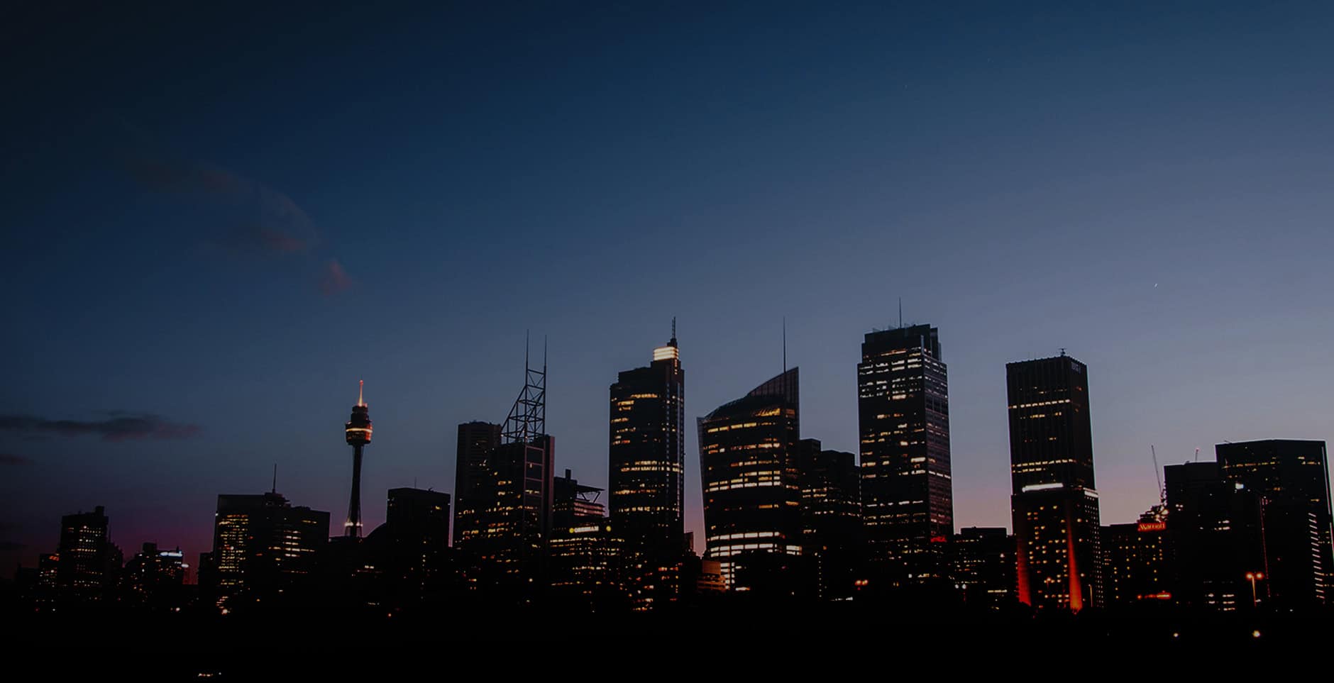 Sydney skyline at dusk with illuminated skyscrapers and the Sydney Tower.