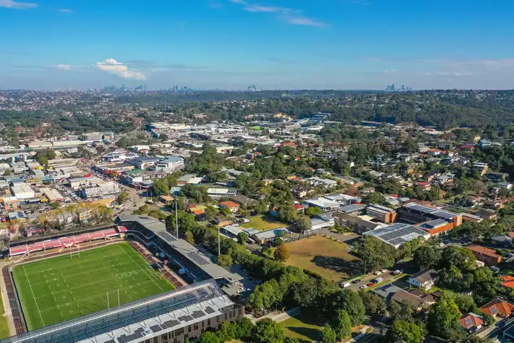 Aerial view of Brookvale with sports fields and residential areas under a blue sky.